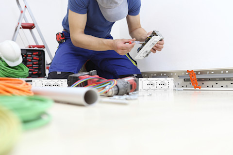 An electrician sits on the floor installing new wiring.