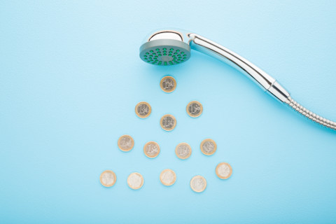 Euro coins as drops falling from shower head on light blue table background. Blue pastel colour background. Closeup. Water consumption and saving concept.