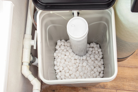 This image shows an automatic water softener system with salt in a plastic tank, installed in a home’s utility area.
