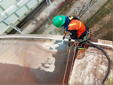 A painter with a green cap sandblasting to remove paint.