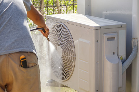 A man cleaning an air conditioner's air duct with water