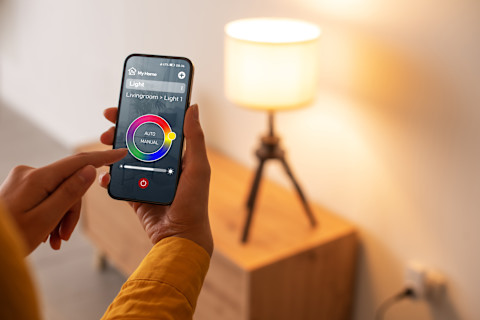 The image shows a person controlling their smart bulb, fitted in a lamp, with a smartphone. 