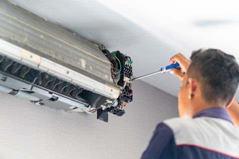 A technician repairing an air conditioning unit, working on the interior components while the unit is open and exposed.