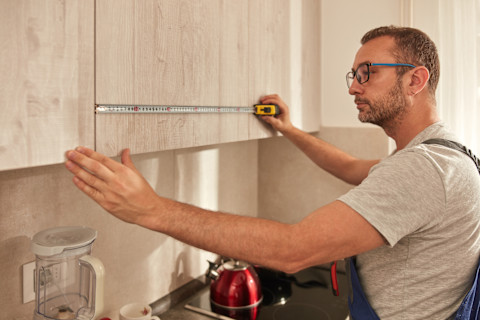 A man measuring cabinets after installation.