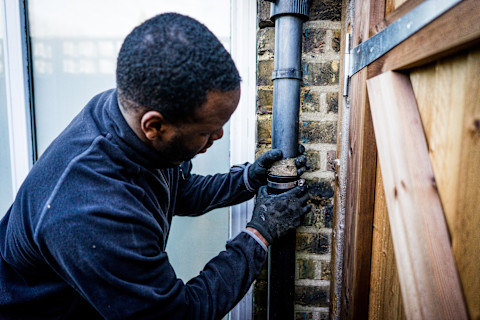 A plumber wearing a jacket fixing a leaked pipe.