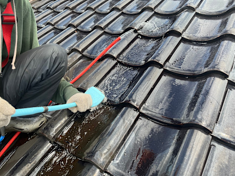 This image shows a tradesperson using a scrubbing brush and a hose to clean roof tiles.