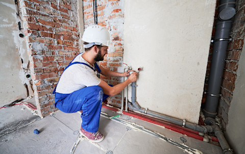 Close-up of a man fixing low water pressure. The image shows the man working on a plumbing fixture or valve, with tools and equipment visible.