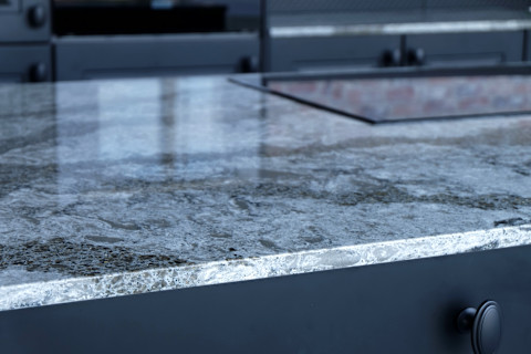 A black quarts worktop in the centre of a modern kitchen setup, sparkling after a clean. The worktop sits on top of a smart black cupboard, with similar cupboards just visible over the worktop in the blurred background.