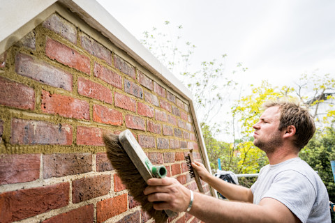 A stonemason cleaning a stone wall with cleaning brushes