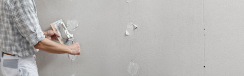 Handyman putting stucco on plasterboard wall using a trowel 