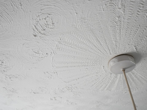 Close-up of a white textured ceiling with circular patterns. A ceiling light fixture is visible, with wires extending downward.