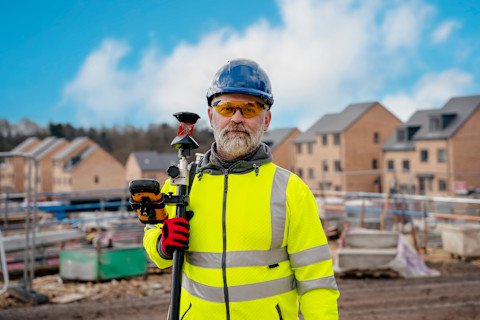Surveyor builder site engineer with theodolite total station at construction site outdoors during surveying work