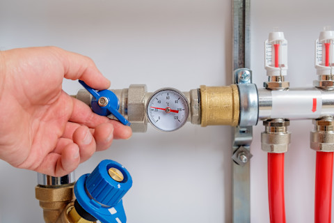 Close-up of a water pressure regulator installed on a plumbing system. The image shows the regulator with a gauge, connected to pipes. The background includes other plumbing components and fixtures.