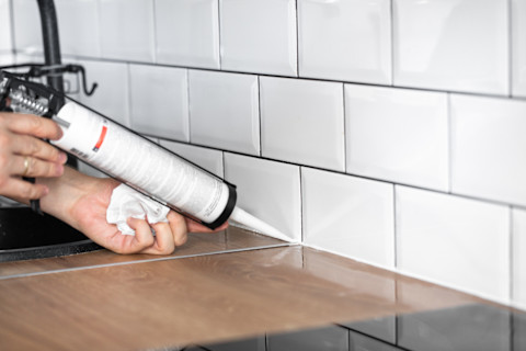 This image shows a tradesperson finishing the tiling of a kitchen.
