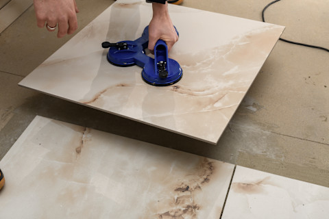 This image shows a close up of a professional tiler laying ceramic tiles on the ground in a bathroom or kitchen.