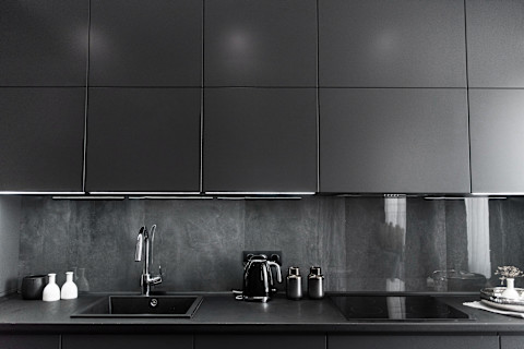 This image shows a modern and stylish kitchen interior featuring sleek grey and black cabinetry, a matching countertop and stainless steel appliances.