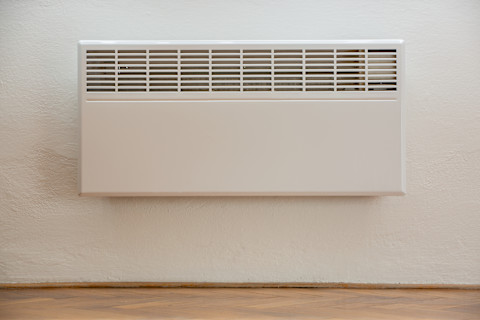 Cream fan assisted radiator on a cream painted wall with wood flooring.