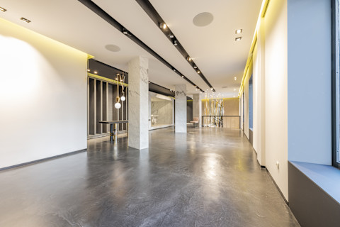 This image shows a grey polished concrete floor in a well-lit commercial space. There are some pendant lights in the background and no furnishings.
