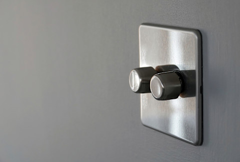 A screwless stainless steel double dimmer light switch mounted on a grey coloured interior wall.