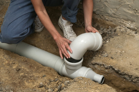 A technician installing a backwater valve in a home's plumbing system, showing the valve being secured into place with pipes and tools nearby.