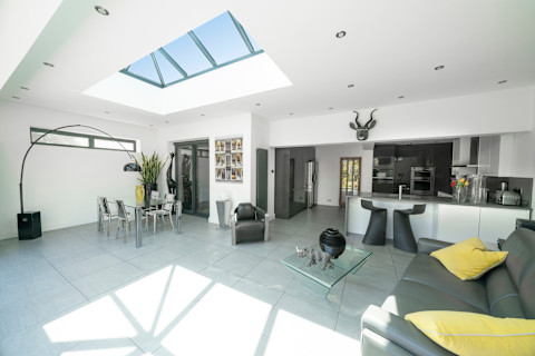 This image shows an open plan living space with a casual seating area and kitchen illuminated by natural light through the Korniche lantern in the ceiling.