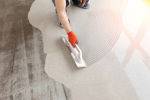 Worker leveling freshly poured screed concrete floor using a trowel for a smooth finish.