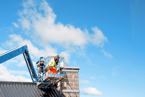 Construction workers operating from a telescopic boom lift while installing insulated panels on the facade of a multistory building.


