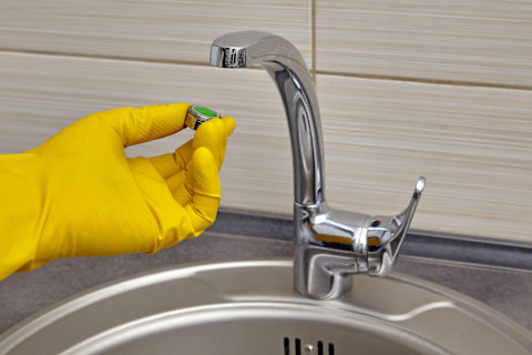 A person installing a kitchen tap aerator, showing hands working on the faucet and the aerator attached to the tap spout.
