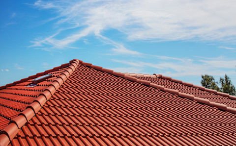 The roof of a house with red clay tiles and a skylight and the sky in the background