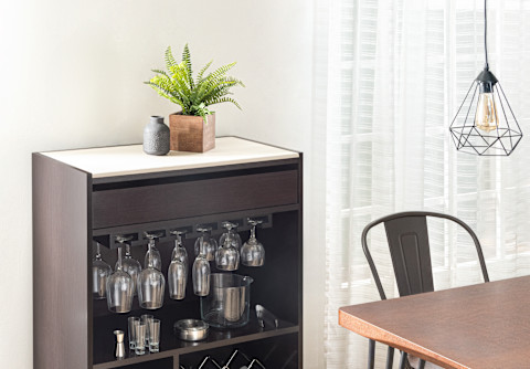 A home bar with some faux plants on top sitting next to a dining table.