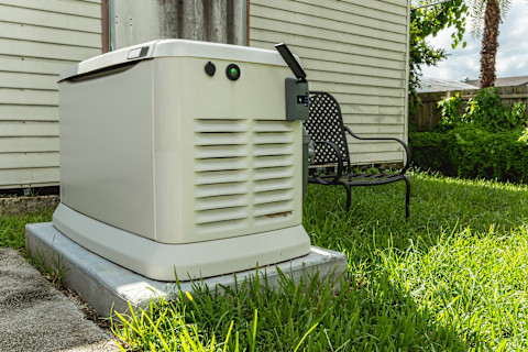 A white colour home generator in a garden next to a black chair.