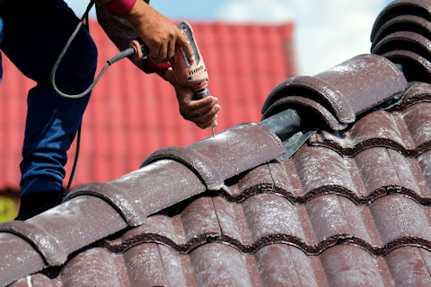 A construction worker installing shingles on a new house roof using a drill