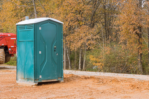 A portable toilets set up at an outdoor event or construction site, clearly visible and positioned on a paved or gravel area.