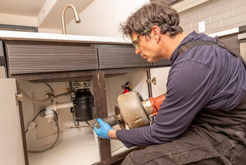 A plumber repairing a garbage disposal.