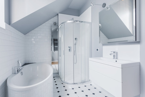 This image shows a small, bright bathroom with classic-modern decor, featuring a white freestanding bathtub, a pedestal sink and soft grey walls.