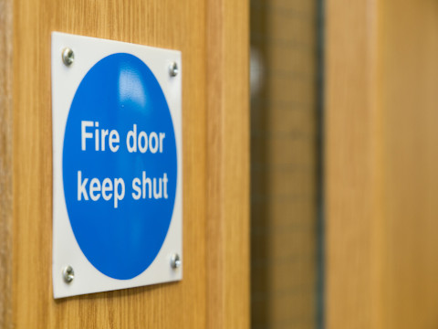Close-up of a blue "Fire Door Keep Shut" sign mounted on a wooden door, highlighting essential fire safety precautions in a building.