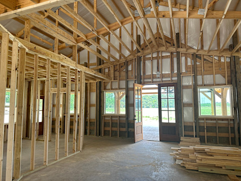 A large pole barn with a metal roof and open sides, featuring a sturdy frame supported by vertical posts, set in an open field or rural area.
