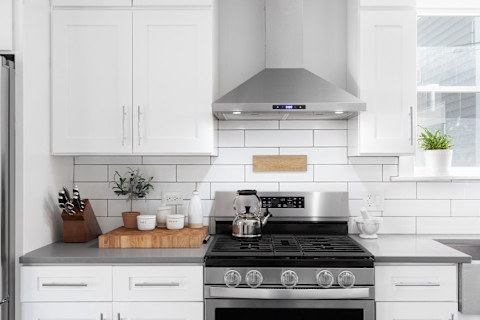 Hand of young cleaning stainless steel kitchen countertop with clean cloth, surrounded by dishes and utensils.