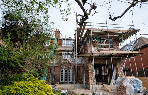 A house extension renovation underway, featuring a three storey brick house with scaffolding around the ongoing extension construction. 