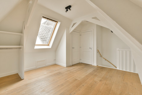An empty room painted white with wood flooring and skylights on the top of the attic. Loft windows are visible in the photo