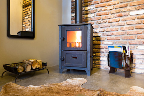 Modern wood burning stove inside cozy living room with rustic brick walls and bear skin on the floor.