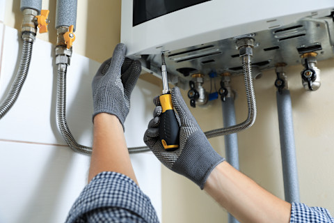 This image shows a heating engineer using a screwdriver to fit or repair a gas boiler in a residential home.