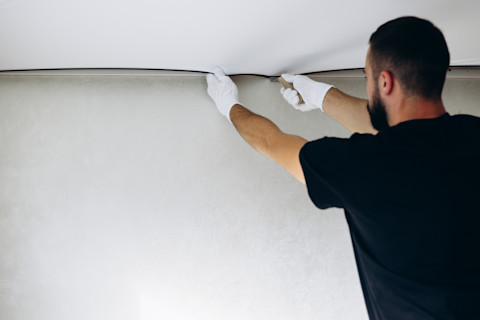 A handyman in white gloves fixing a stretched ceiling