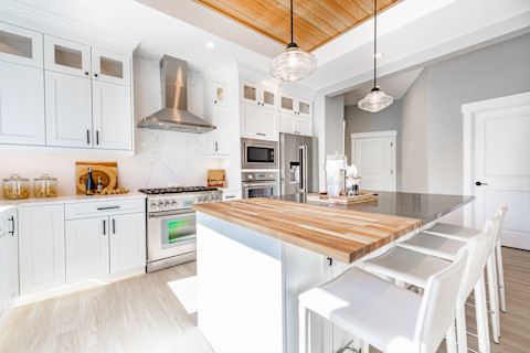 Close-up of a butcher block countertop in a kitchen. The image shows the warm, wooden surface with visible grain patterns, integrated into cabinetry. The background includes kitchen appliances and other countertop items.