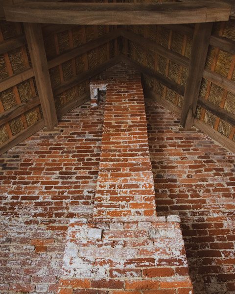 A very old brick wall and chimney breast leading up to a traditional thatched roof.