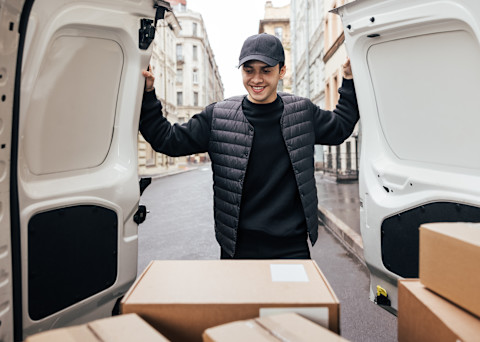 This image shows boxes in the back of a white transit-style van. The man who owns the vehicle is closing the back doors while smiling.