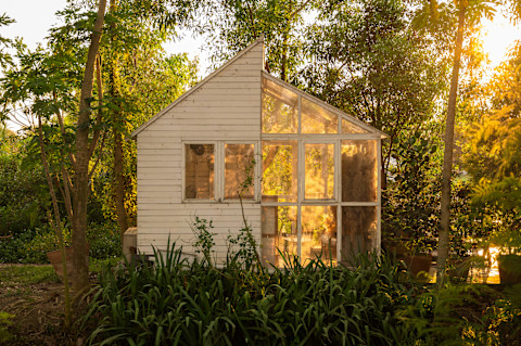 A light and airy furnished sun room in an English country style garden, in the evening, with the setting sun in the background.