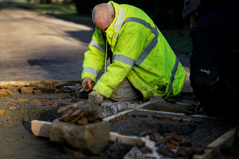 Workman in hi-vis jacket using a hammer on a concrete driveway