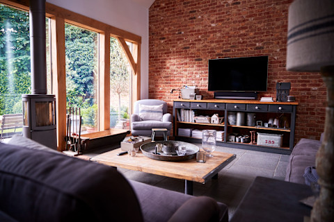 Cosy living room with an exposed brick wall, large windows, and a wood-burning stove. 