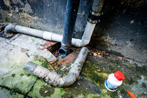 This image shows the replacement of a drain pipe. The new part has been fitted and the old, worn original part is to the side of the image.